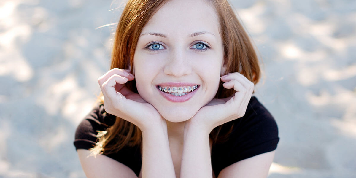 Smiling young lady in braces holding her face in both hands